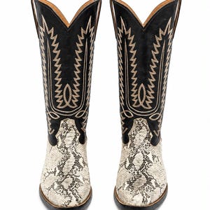 Puede incluir: Un par de botas de estilo vaquero en blanco y negro con el pie estampado de piel de serpiente y una caña alta negra. La caña está decorada con intrincadas costuras de color tostado en un patrón geométrico dentado y tiene punta afilada.