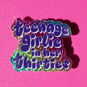 May include: A rainbow holographic sticker with the text "teenage girlie in her thirties".