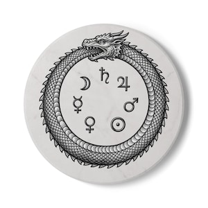 Puede incluir: Un posavasos redondo y blanco con una ilustración negra de un ouroboros, un dragón comiendo su cola, rodeando símbolos astrológicos. El posavasos tiene una textura similar al mármol.