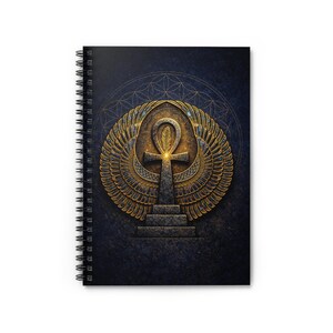 May include: Spiral-bound notebook featuring a detailed illustration of an Ankh symbol with golden wings and accents. The design is set against a dark blue textured background with a subtle geometric pattern, creating a striking contrast.