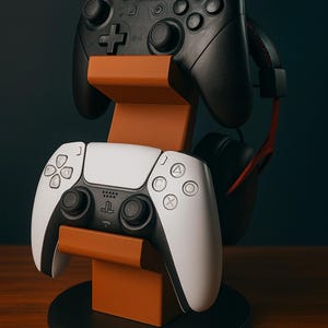 May include: A two-tiered stand for gaming controllers, in brown and black. It holds a black Nintendo Switch controller, a white and black PlayStation 5 controller, and a black headset with red detailing. The stand sits on a black circular base.