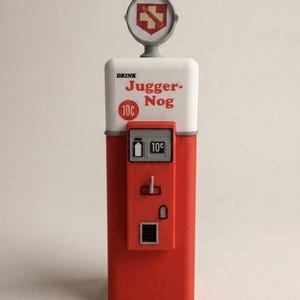 May include: A red and white novelty drink dispenser with the text "DRINK JUGGER-NOG 10¢". The dispenser has a circular emblem on top and a small display window. The design is reminiscent of a vintage vending machine.