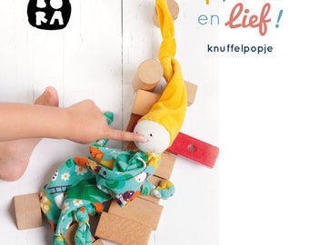 May include: A yellow and white plush toy with a green and white patterned fabric. The toy is sitting on top of wooden blocks. The text "Hip, STOER en lief!" is written in blue and white. The text "knuffelpopje" is written in black. The text "Deborah van de Leijgraaf by-bora.com" is written in black.