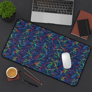 May include: A blue desk mat with a colourful abstract pattern. The mat has a black border and a white computer mouse is on the mat.