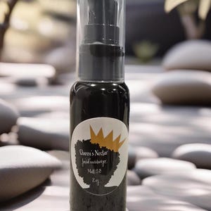 Peut inclure: Une bouteille noire avec un distributeur à pompe transparent et une étiquette noire et dorée qui indique "Queen's Nectar Facial Moisturizer Matt. 5.8 2 oz."