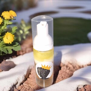 Puede incluir: Una botella de plástico transparente con una etiqueta amarilla y marrón. La etiqueta dice "Queen's Water Foaming Face Wash" y "Net 58 2 fl oz".