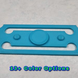 May include: A light blue plastic fidget toy with a round spinning center and two smaller buttons on either side. 13+ Color Options.