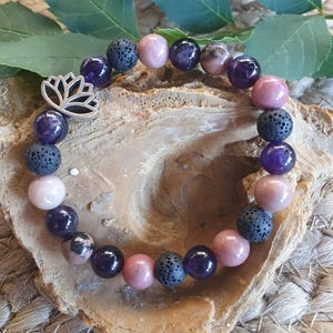 May include: A bracelet with a silver lotus charm, made with a variety of gemstone beads. The beads are in shades of purple, pink, and black. The bracelet is designed in a circular pattern, creating a fashionable accessory.