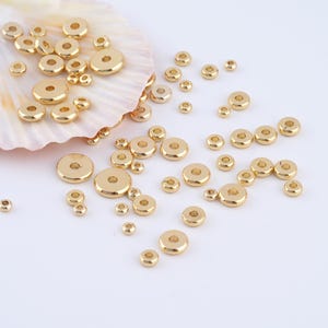 May include: A large quantity of gold-colored metal spacer beads. The beads are round with a hole in the center. They are scattered on a white surface.