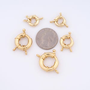 May include: Five gold-toned metal ring clasps for jewelry making. The clasps are round and have a diameter of about 1 inch. The clasps are shown next to a US quarter for size comparison.