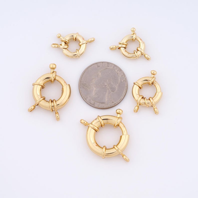 May include: Five gold-toned metal ring clasps for jewelry making. The clasps are round and have a diameter of about 1 inch. The clasps are shown next to a US quarter for size comparison.