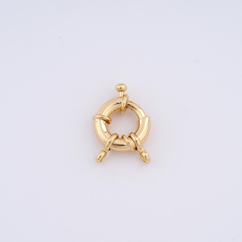 May include: Gold-toned metal ring clasp with two loops. The ring is round and has a textured surface. The loops are attached to the ring at opposite ends.