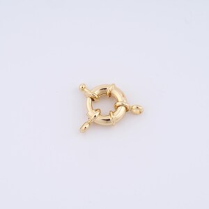 May include: Gold-toned metal ring clasp with three loops. The ring is round and has a smooth surface. The loops are attached to the ring at three points.