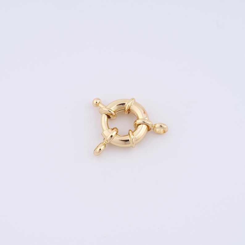 May include: Gold-toned metal ring clasp with three loops. The ring is round and has a smooth surface. The loops are attached to the ring at three points.