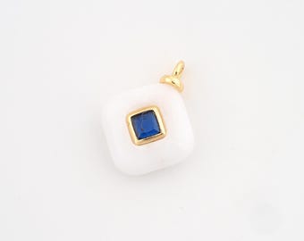 May include: A white pendant with a square, blue gemstone set in a gold frame. The pendant has a rounded square shape and a small gold loop at the top for a chain. The gemstone is a deep blue colour.
