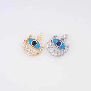 May include: Two pendant charms featuring an eye design within a crescent moon shape. One charm is gold-toned with clear crystals and a blue eye. The other is silver-toned with a blue eye and clear crystals.