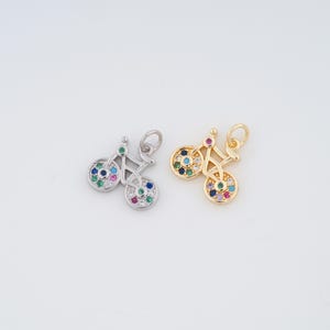 May include: Two silver and gold bicycle charms with colorful gemstones. The charms are detailed with a small handlebar and two wheels.