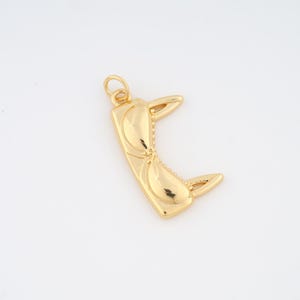 May include: A gold-colored pendant in the shape of sunglasses. The pendant has a rectangular frame with curved lenses and a small loop at the top for a chain. The sunglasses are detailed with a textured design.