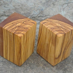 May include: Two wooden salt and pepper shakers made from olive wood. The shakers are square shaped and have a natural wood finish.