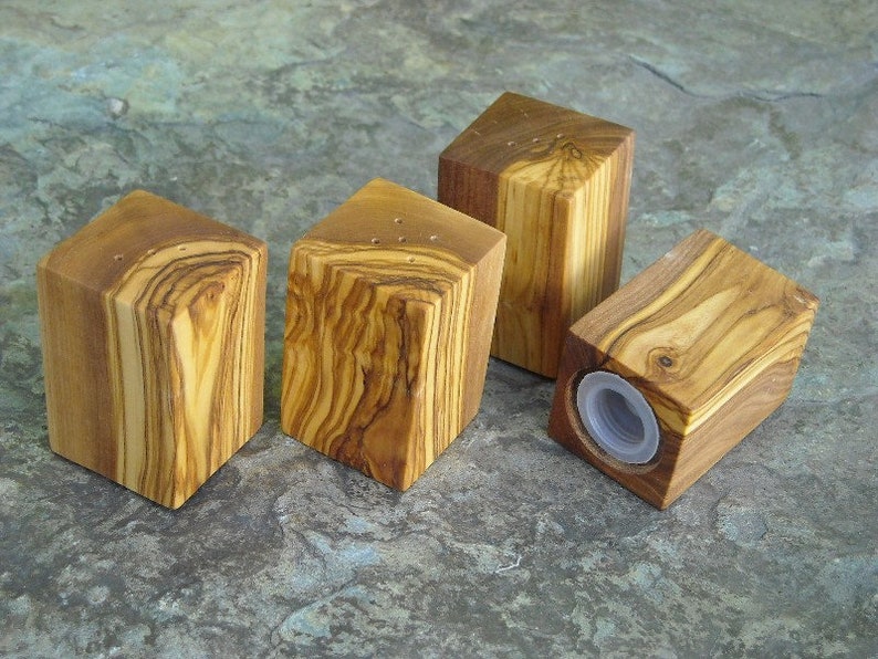 May include: Four wooden salt and pepper shakers made from olive wood. The shakers are square and have a natural wood finish.