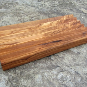 Puede incluir: Una bandeja de servir de madera con un borde ondulado y un acabado de veta de madera natural. La bandeja est&aacute; hecha de madera de olivo y tiene una forma rectangular.