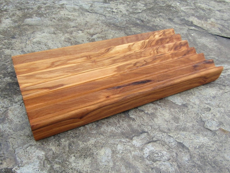 Puede incluir: Una bandeja de servir de madera con un borde ondulado y un acabado de veta de madera natural. La bandeja est&aacute; hecha de madera de olivo y tiene una forma rectangular.