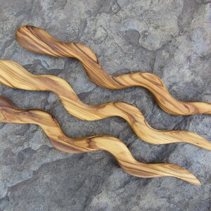 Puede incluir: Tres palos de pelo de madera con un dise&ntilde;o ondulado. Los palos son de madera de olivo y tienen un color marr&oacute;n natural.
