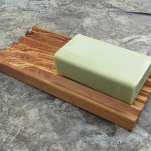 Puede incluir: Un jabonera de madera con un dise&ntilde;o acanalado para ayudar a drenar el agua. Una barra de jab&oacute;n verde descansa sobre la jabonera.