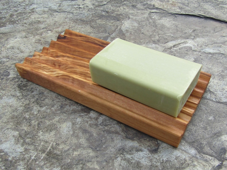 Puede incluir: Un jabonera de madera con un dise&ntilde;o acanalado para ayudar a drenar el agua. Una barra de jab&oacute;n verde descansa sobre la jabonera.