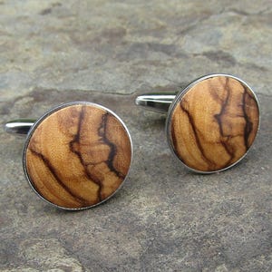 May include: A pair of silver cufflinks with round wooden inlays. The wood has a natural brown and black grain pattern.