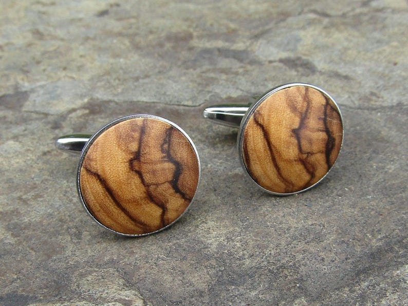 May include: A pair of silver cufflinks with round wooden inlays. The wood has a natural brown and black grain pattern.