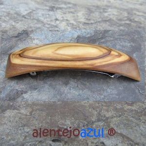 May include: A wooden hair clip with a natural wood grain finish. The clip is curved and has a silver metal clasp.