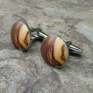 May include: A pair of cufflinks with a round, wooden design. The wood is a light brown with darker brown streaks. The cufflinks are made of silver metal.