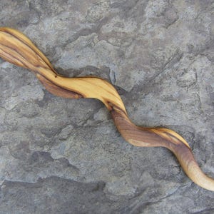 Puede incluir: Un palo de pelo de madera con un acabado de grano de madera natural. El palo es curvo y tiene una superficie lisa y pulida.