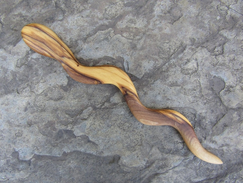 Puede incluir: Un palo de pelo de madera con un acabado de grano de madera natural. El palo es curvo y tiene una superficie lisa y pulida.