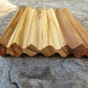 Puede incluir: Un jabonera de madera con un dise&ntilde;o ondulado. La jabonera est&aacute; hecha de madera clara y oscura, creando un patr&oacute;n a rayas.
