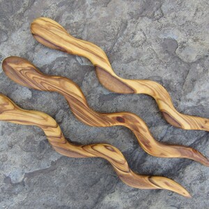 Puede incluir: Tres peines de madera para el cabello con un dise&ntilde;o ondulado y serpentino. Los peines est&aacute;n hechos de madera de olivo y tienen un color marr&oacute;n claro natural.