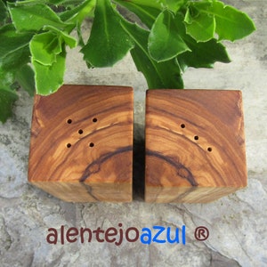 Op de afbeelding: Een set van twee houten zout- en peperstrooiers gemaakt van olijfhout. De strooiers zijn vierkant en hebben een natuurlijke houtkleur. Elke strooier heeft vijf gaten aan de bovenkant om zout en peper te strooien.
