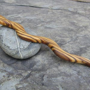 Puede incluir: Un palo de pelo de madera con un patr&oacute;n de veta de madera natural. El palo es curvo y tiene un acabado liso.