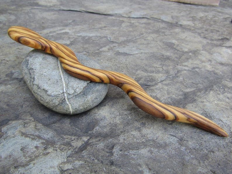 Puede incluir: Un palo de pelo de madera con un patr&oacute;n de veta de madera natural. El palo es curvo y tiene un acabado liso.