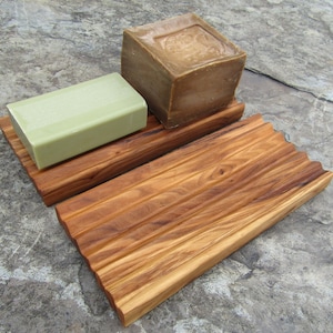 Puede incluir: Un jabonera de madera con dos barras de jab&oacute;n. Una barra es verde y la otra es marr&oacute;n.