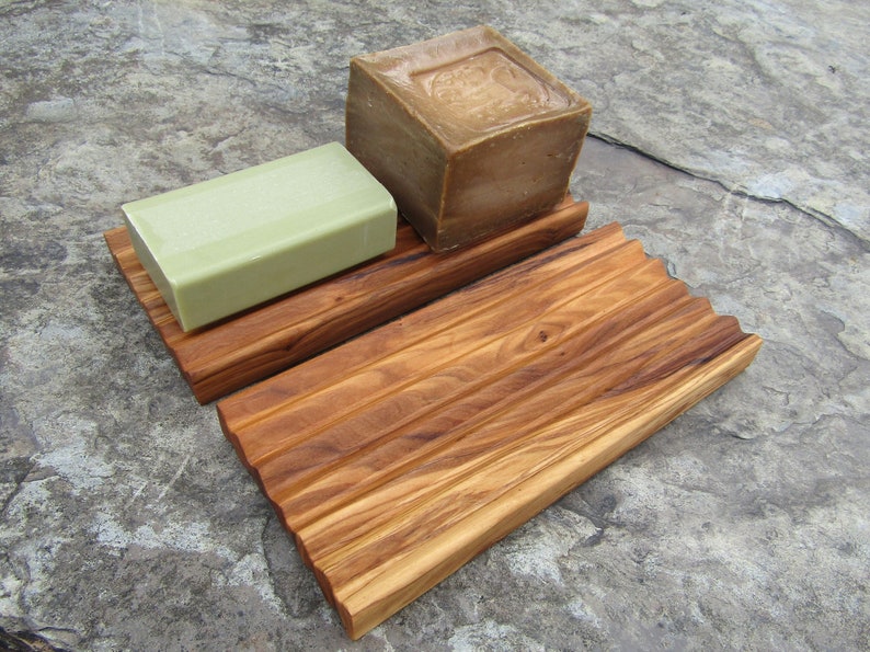 Puede incluir: Un jabonera de madera con dos barras de jab&oacute;n. Una barra es verde y la otra es marr&oacute;n.