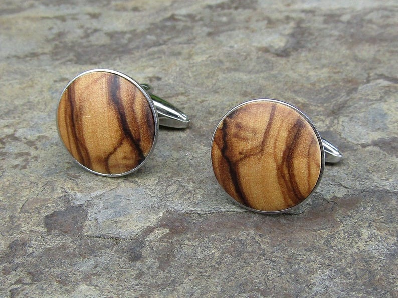 May include: A pair of cufflinks with a round, wooden design. The wood is a light brown colour with dark brown streaks. The cufflinks are made of silver metal.