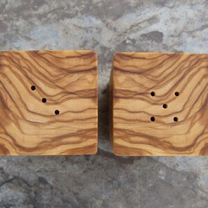 Op de afbeelding: Twee houten zout- en peperstrooiers met een natuurlijke houtnerf afwerking. Elke strooier heeft vier gaten om zout en peper te strooien.