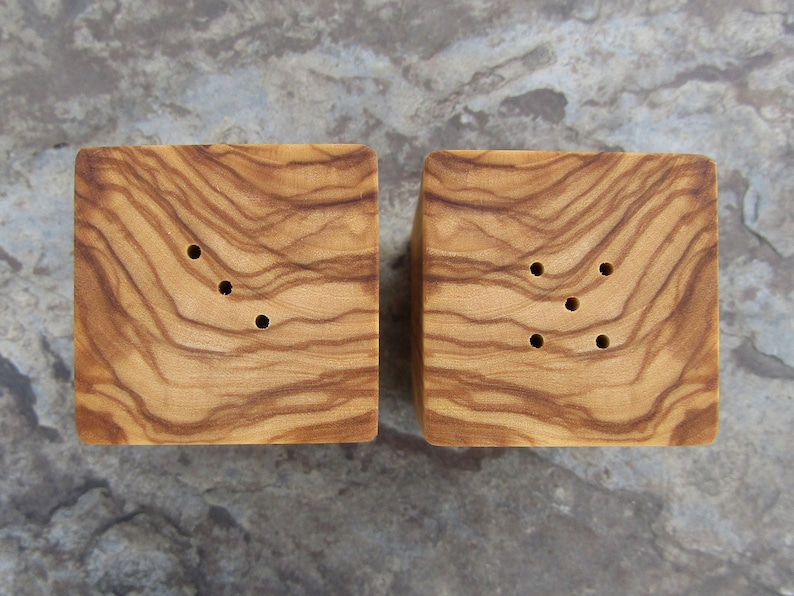 Op de afbeelding: Twee houten zout- en peperstrooiers met een natuurlijke houtnerf afwerking. Elke strooier heeft vier gaten om zout en peper te strooien.