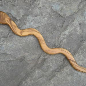 Puede incluir: Un palito para el pelo de madera con forma de serpiente, con un acabado de madera natural.
