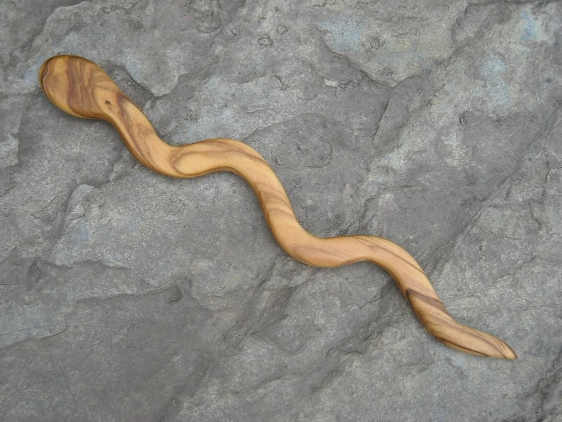 Puede incluir: Un palito para el pelo de madera con forma de serpiente, con un acabado de madera natural.