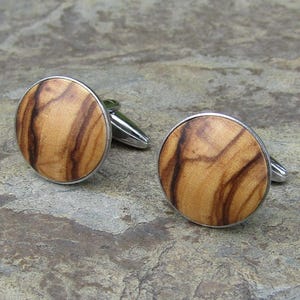 May include: A pair of cufflinks with a wood grain design. The cufflinks are round and have a silver metal frame.