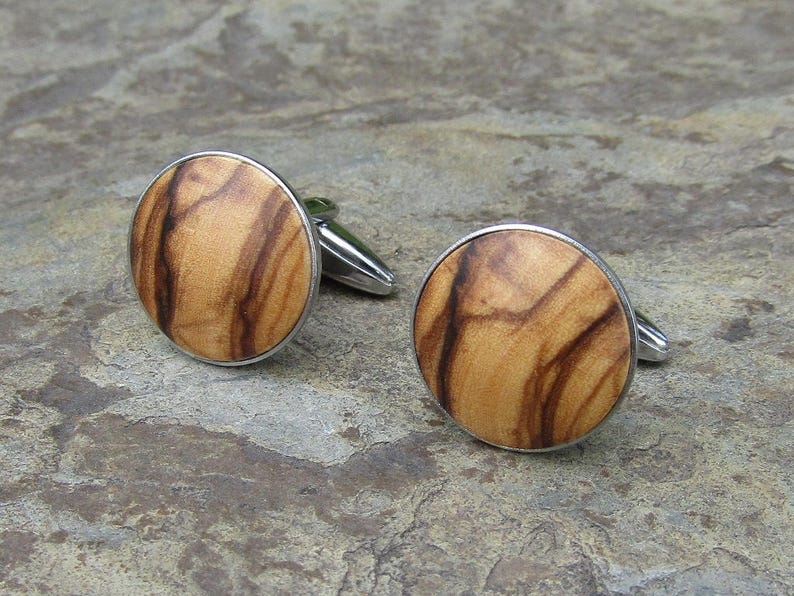 May include: A pair of cufflinks with a wood grain design. The cufflinks are round and have a silver metal frame.