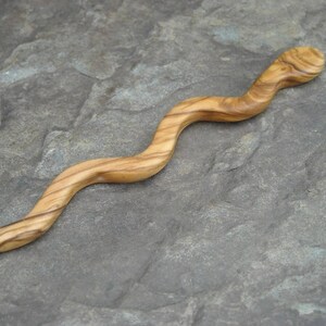 Puede incluir: Un palo de pelo de madera en forma de serpiente con un acabado de grano de madera natural. El palo es curvo y tiene una superficie lisa y pulida.